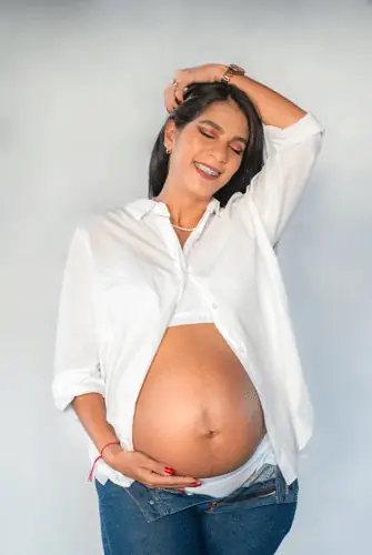 Sesión de maternidad: mujer embarazada sonriendo con camisa blanca