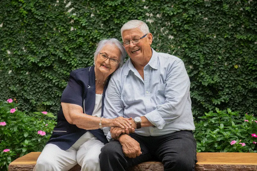 Pareja de adultos mayores sonriendo abrazados en un jardín