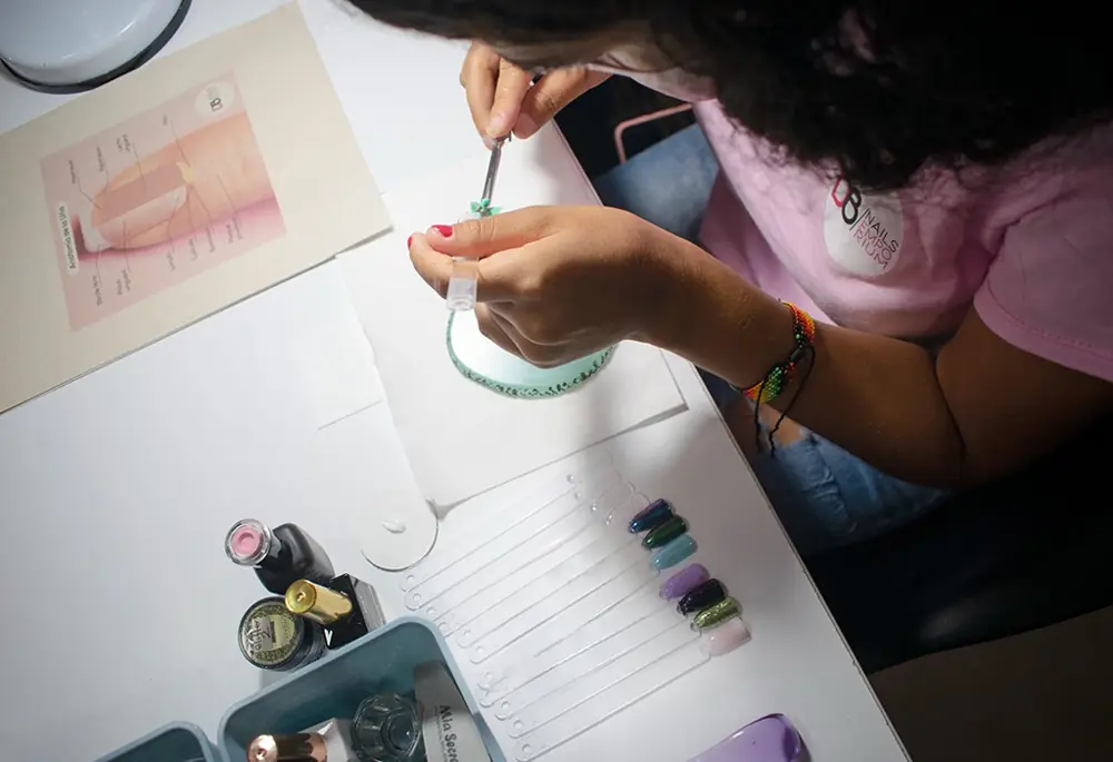 Manicurista pintando uñas de muestra en su mesa de trabajo, vista desde arriba